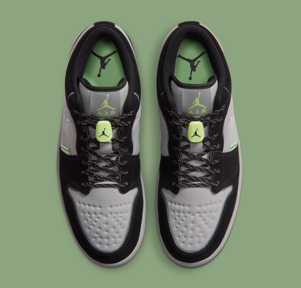 Vista superior del par de Air Jordan 1 Low Light Smoke Grey Barely Volt sobre fondo verde, con las plantillas verdes con el Jumpman, las trabas flúor y los cordones negros con puntos claros