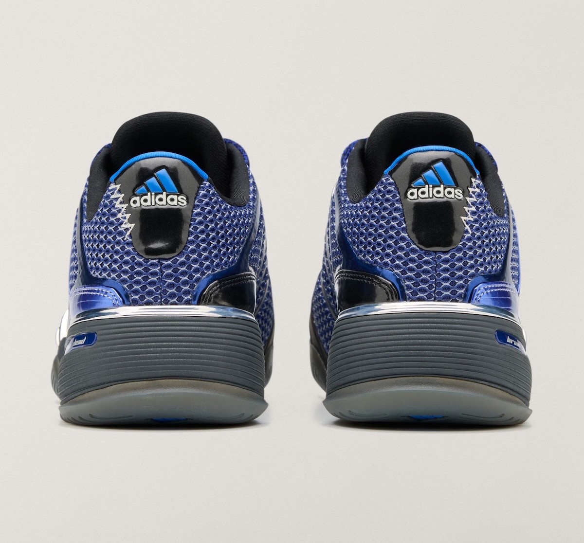 Vista trasera del par del Brain Dead x adidas Barricade V Mystery Ink sobre fondo gris claro, con malla azul, talón negro con el logo de adidas en azul y blanco, detalles azules brillantes y suela gris oscura con base translúcida
