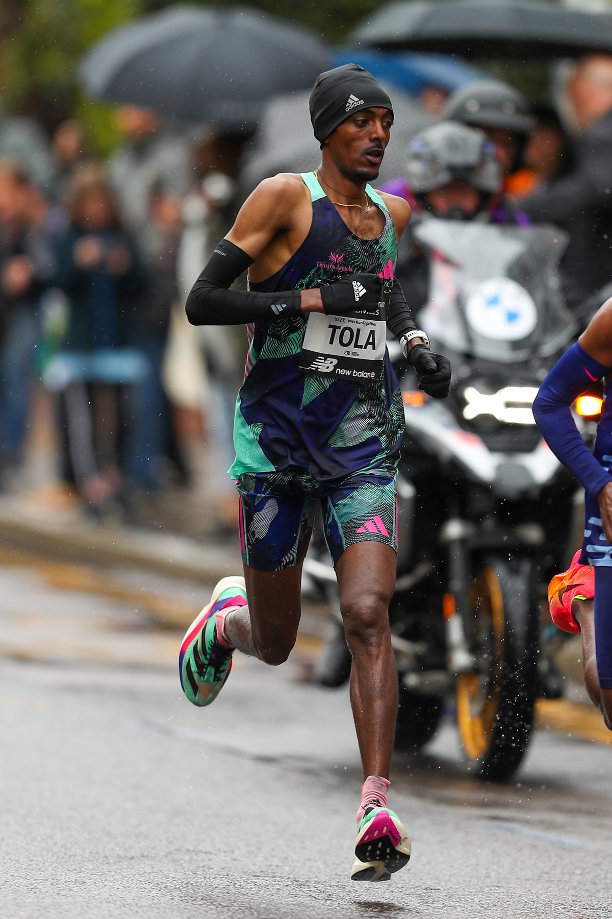 Foto de archivo: Tamirat Tola, con musculosa oscura, gorro negro y número con su apellido, corre bajo la lluvia en el Maratón de Londres 2023, seguido por una moto