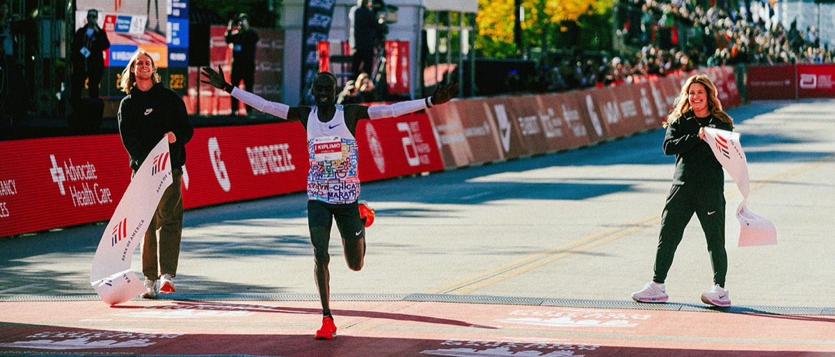 Foto de archivo: Jacob Kiplimo, con la musculosa blanca de la carrera, abre los brazos al cruzar la meta del Maratón de Chicago 2025 mientras dos voluntarios sostienen la cinta