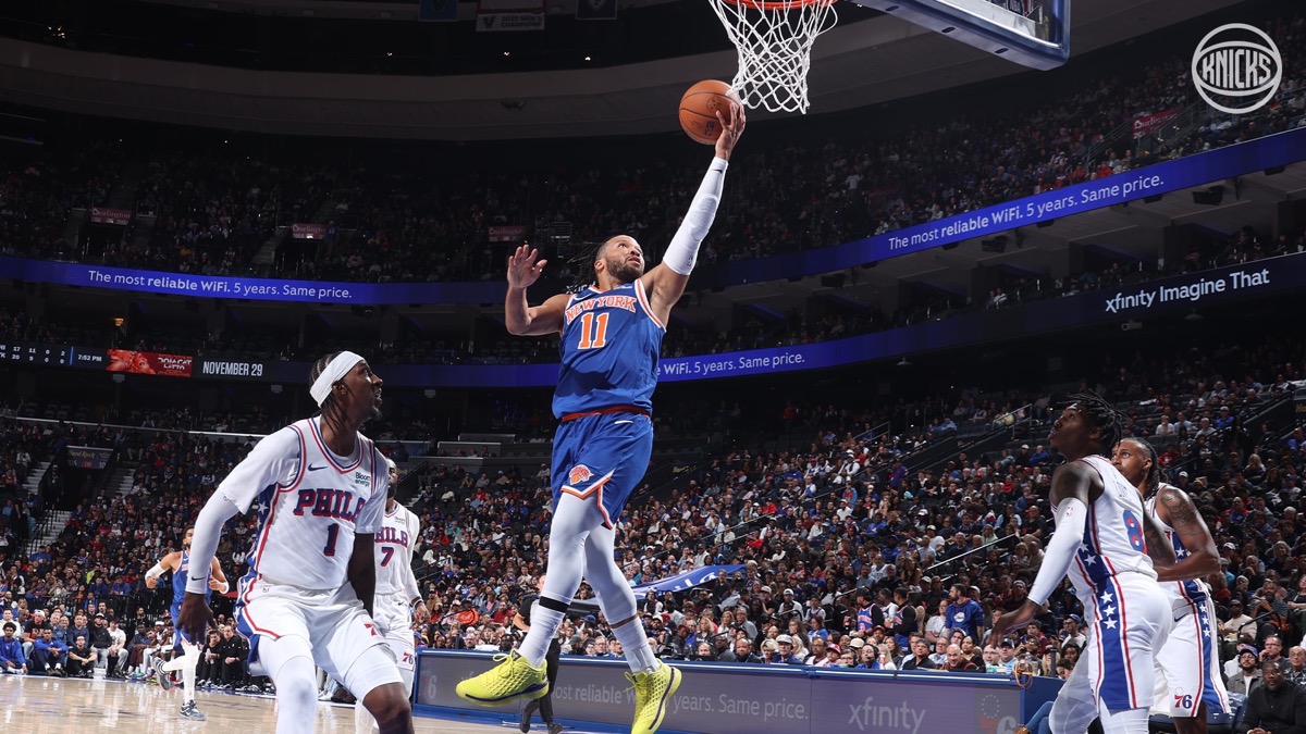 Jalen Brunson, con la camiseta azul número 11 de los Knicks, entra en bandeja ante jugadores de los 76ers vestidos de blanco en el Xfinity Mobile Arena de Philadelphia