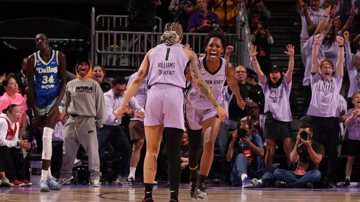 Gabby Williams, de espaldas con la camiseta 1 de Golden State Valkyries, festeja con una compañera mientras el público celebra de pie y una jugadora de Dallas Wings camina detrás