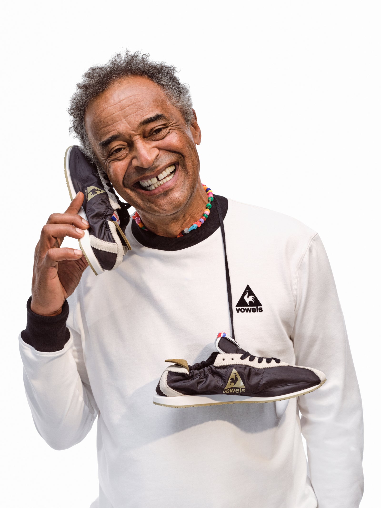 Yannick Noah sonriendo con un par de vowels x Le Coq Sportif Wendon y un buzo blanco de la colección