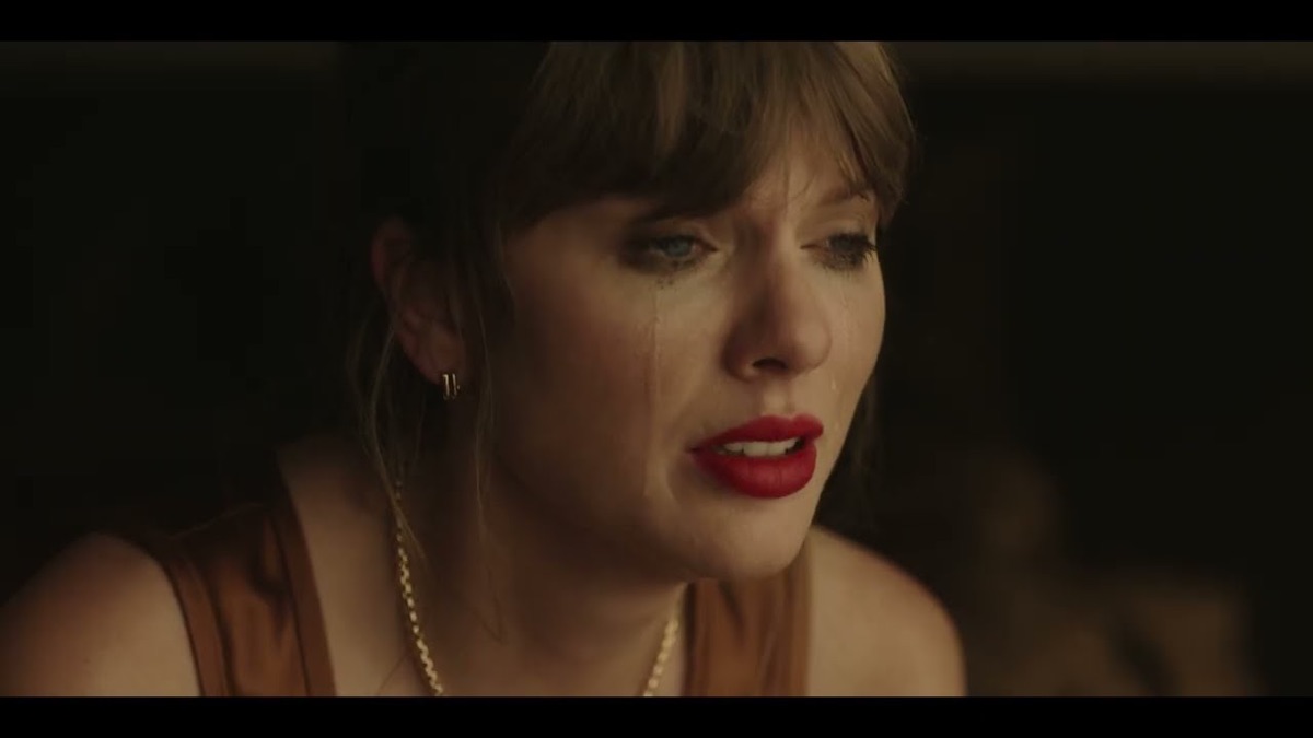 Fotograma del video oficial de "Patient Zero": Taylor Swift en primer plano, con flequillo, labios rojos, aros dorados y lágrimas en la cara, sobre un fondo oscuro