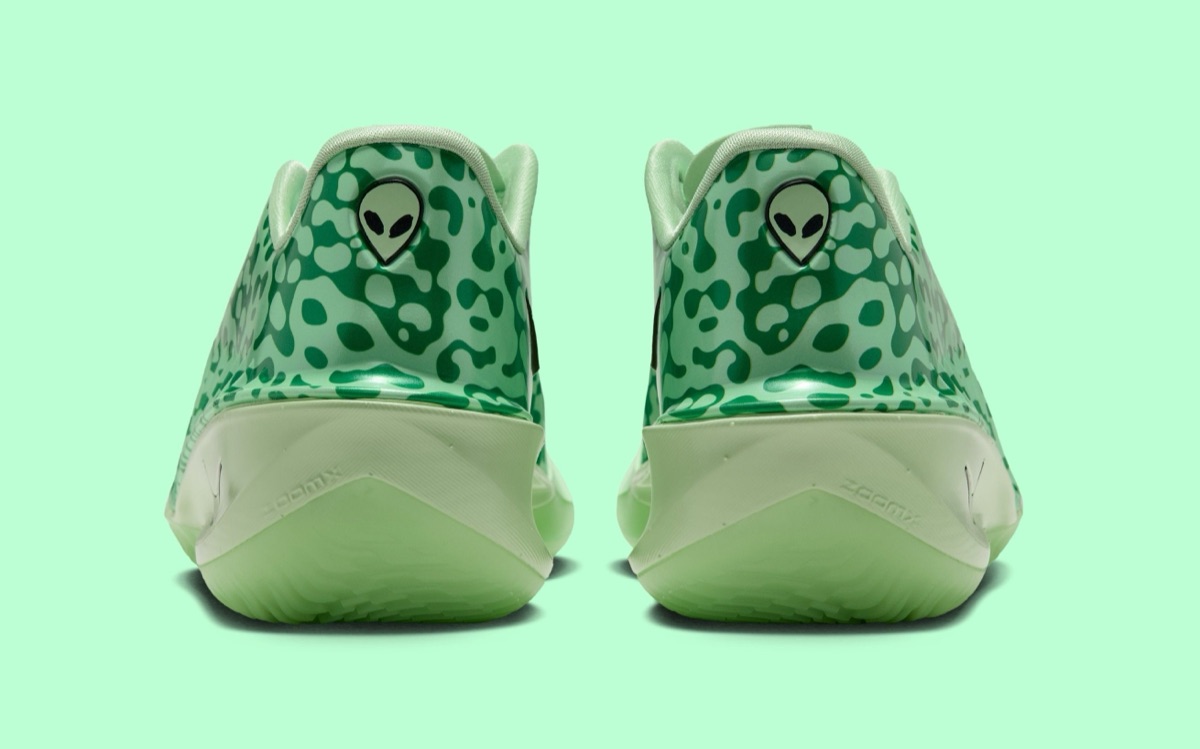 Vista trasera del par del Nike GT Cut 4 Halloween sobre fondo verde agua, con los talones de acabado brillante cubiertos de manchas verde oscuro sobre verde claro, un logo con la cabeza de un alien en cada uno y la mediasuela verde pálido con la palabra ZoomX grabada