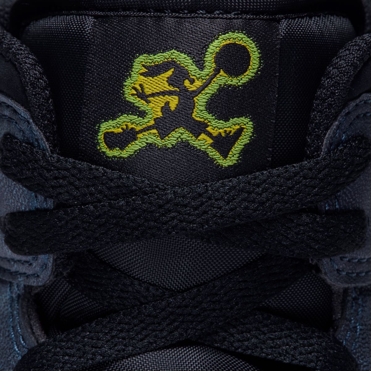 Primer plano de la lengüeta negra del Air Jordan 1 Mid SE de Space Jam con el logo de Bugs Bunny en pose de Jumpman bordado en amarillo con contorno verde, y los cordones negros cruzados adelante