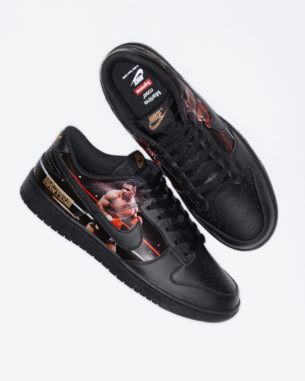 Par del Supreme x Martine Rose x Nike Dunk Low Tyson visto desde arriba sobre fondo blanco, con un zapato mostrando la plantilla negra con los logos de Nike, Supreme y Martine Rose, la etiqueta dorada de Nike en la lengüeta y el otro de costado con la foto de Tyson y las letras doradas