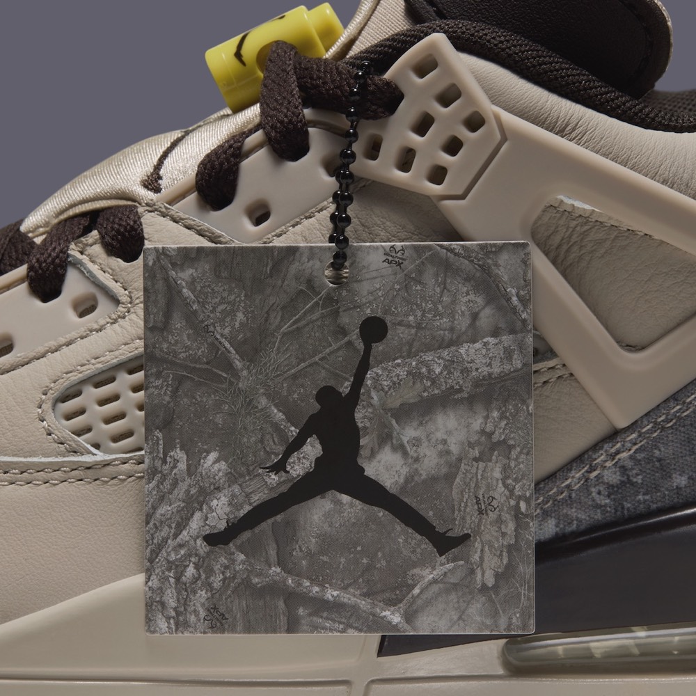 Primer plano del costado del Jordan Spizike Low Realtree Camo con un colgante cuadrado de camuflaje gris y Jumpman negro sujeto a los cordones marrones, junto a las alas crema y la traba de cordones amarilla