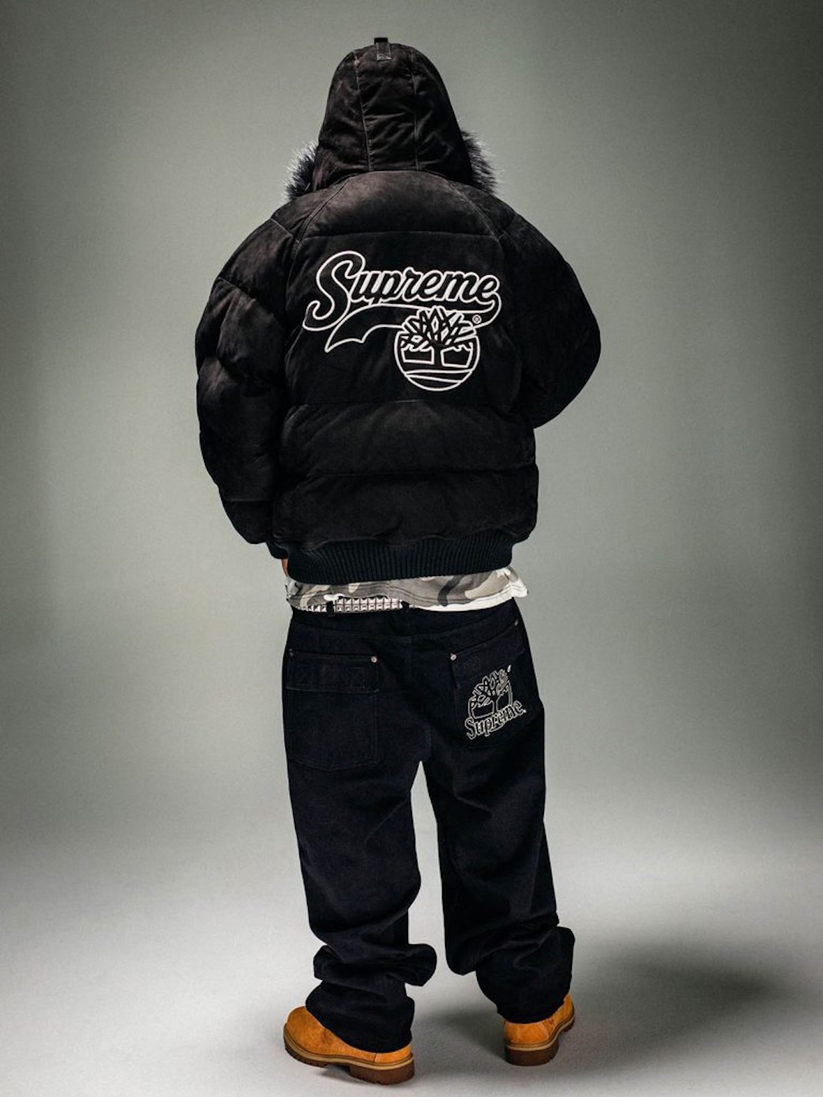 Modelo de espaldas con la campera Supreme x Timberland Suede Puffer negra, con el logo de Supreme y el árbol de Timberland en la espalda