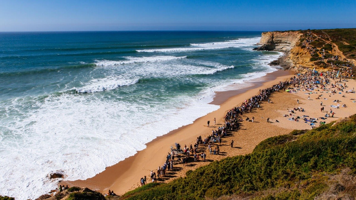 Foto de archivo: vista desde el acantilado de la playa de Ribeira d'Ilhas, en Ericeira, con público sobre la arena y series de olas entrando