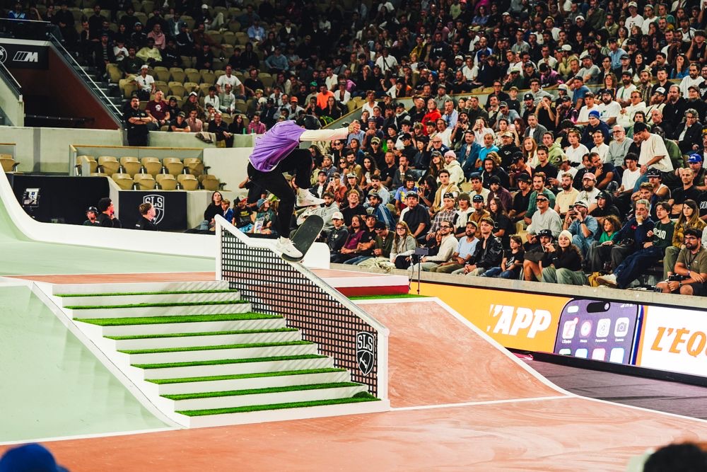 Nyjah Huston, con remera violeta, desliza la tabla sobre la baranda de la escalera del parque armado en Roland-Garros, con la tribuna llena detrás