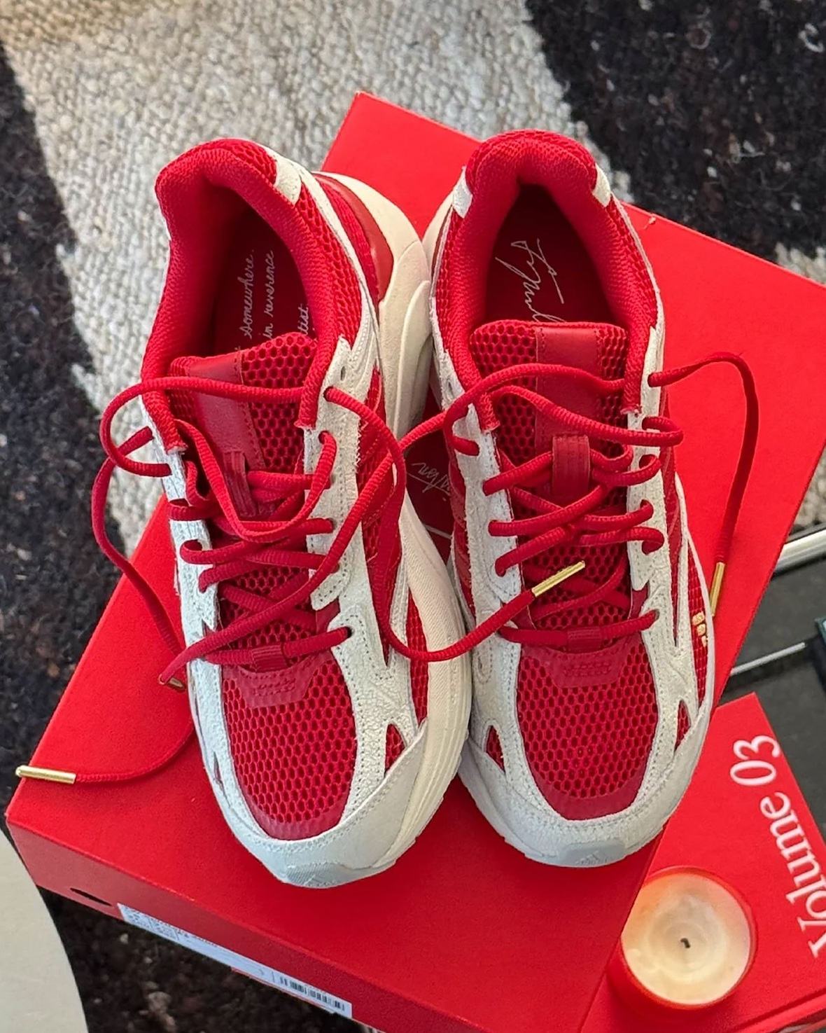 Par de Tyrrell Winston x adidas Spiritain 2000 visto desde arriba sobre una caja roja, con cordones rojos de puntas doradas, capas crema y la firma del artista en la plantilla