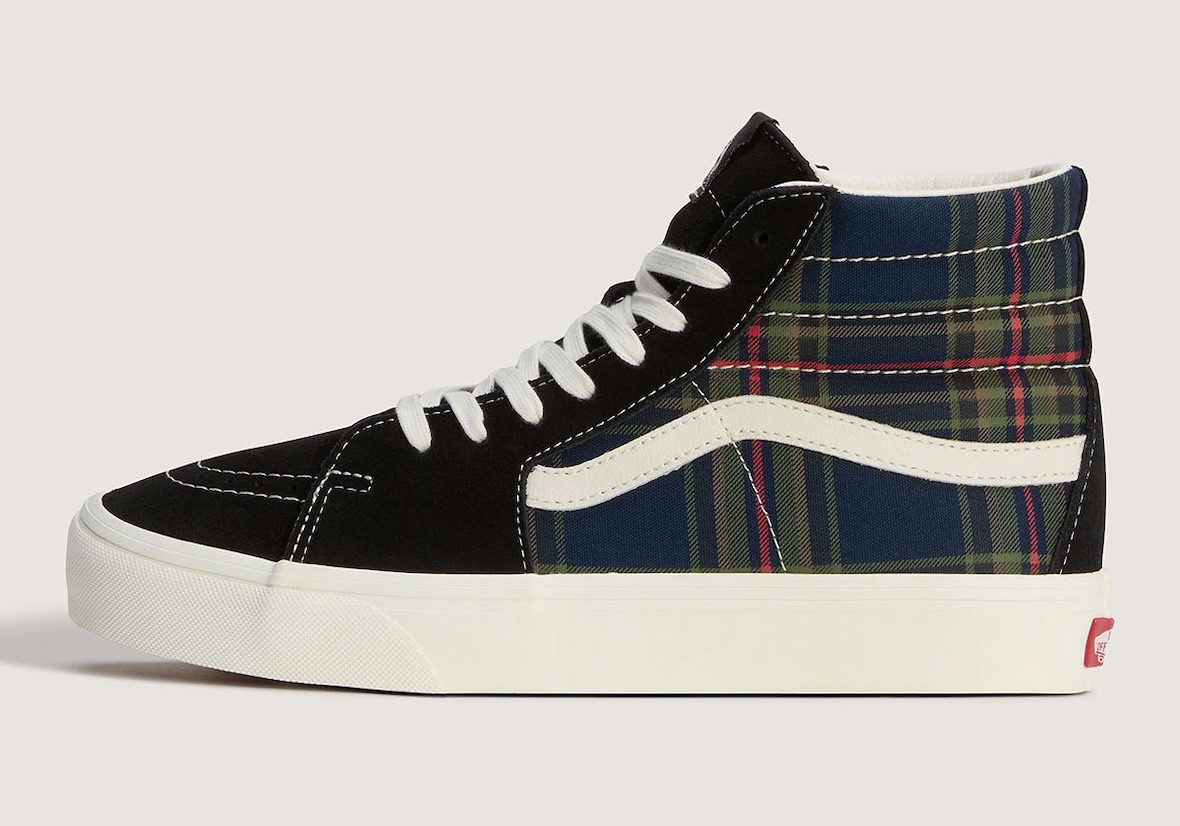 Vans Sk8-Hi Plaid Black/Multi de perfil sobre fondo crema, con gamuza negra en la punta y el empeine, caña de cuadros azul marino con líneas verdes y rojas, Sidestripe crema, cordones blancos, costuras blancas a la vista y suela crema con la etiqueta roja de Vans en el talón