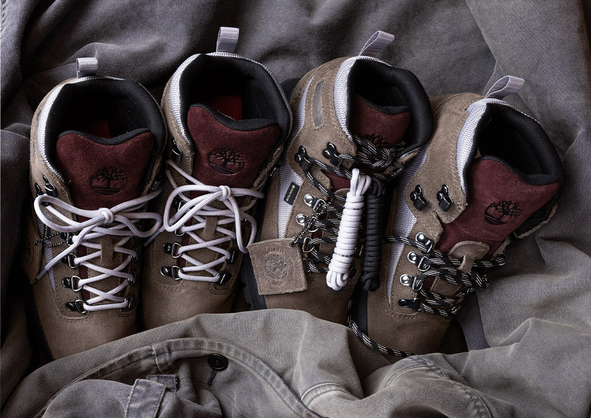 Dos pares del Victor Kan x Timberland Euro Hiker Gore-Tex sobre una tela gris arrugada, en gamuza taupe con lengüeta bordó y logo del árbol en relieve, malla gris clara, ganchos metálicos, cordones gris claro en un par y cordones negros con blanco en el otro, con un juego de cordones extra enrollado y una etiqueta de gamuza colgando