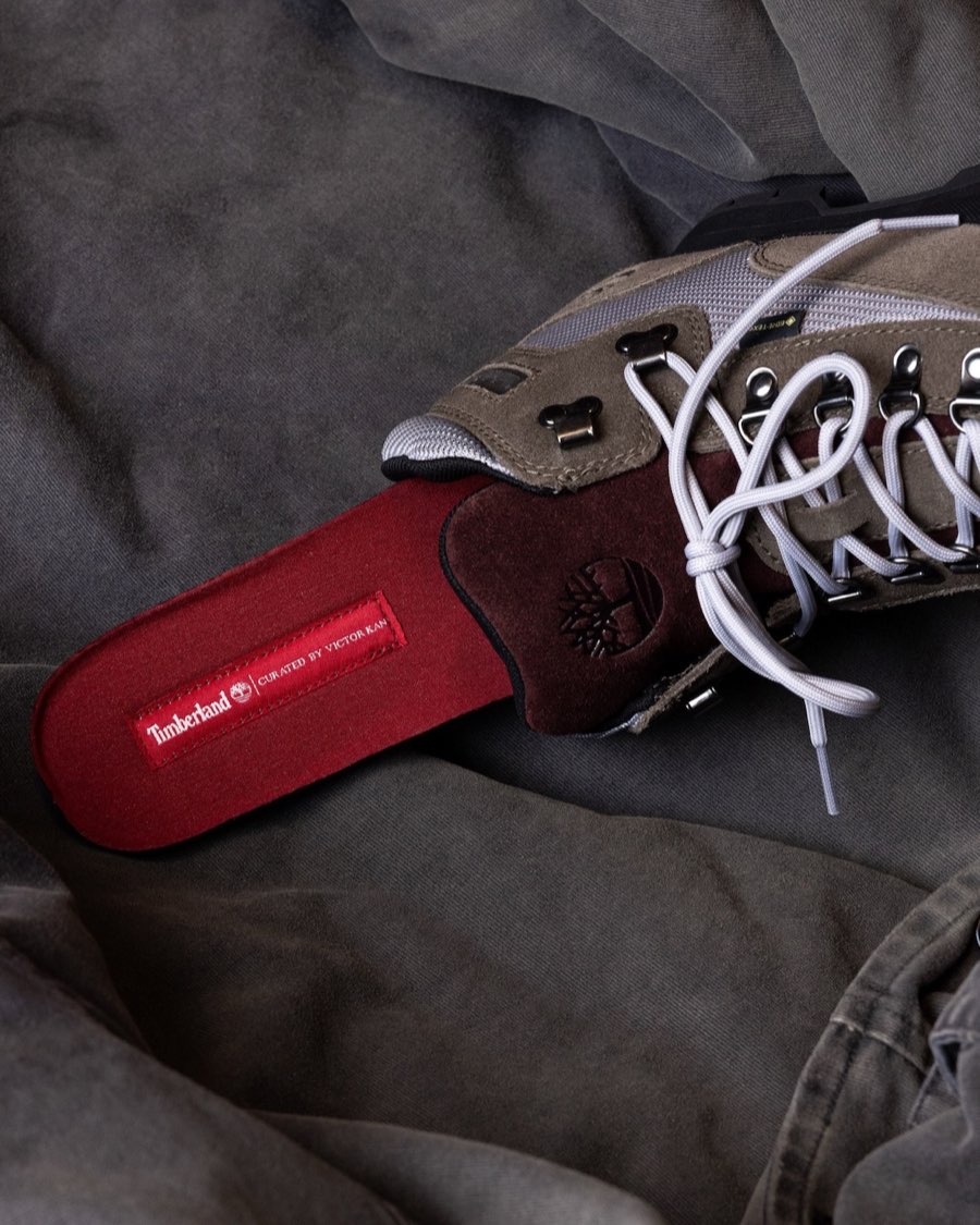 Plantilla roja del Victor Kan x Timberland Euro Hiker asomando de la bota, con la etiqueta Timberland y la leyenda Curated by Victor Kan, junto a la lengüeta de gamuza bordó con el árbol en relieve y cordones gris claro, sobre una tela gris